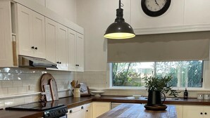A kitchen with white cabinets, a wooden island with stools, a hanging pendant light, and a clock on the wall. - When a little white house in the country is all that is required! (Maffra)