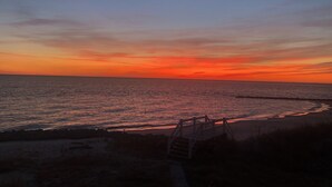 Eine Strandansicht mit einer Holzpromenade, die zum Meer führt, unter einem Sonnenuntergangshimmel.