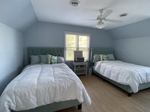 Une chambre avec deux lits, un ventilateur de plafond et une fenêtre avec des stores.