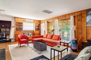 A cozy living room with a red sofa, a black coffee table, and a red armchair. There is a wooden bookshelf, a mirror, and a drum set against the wall. - True Seattle, Mt Baker neighborhood Home 5 beds and 5 TVs (Seattle)