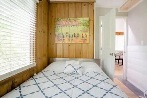 A bedroom with a bed, wooden paneling, a painting, and a window with blinds. - True Seattle, Mt Baker neighborhood Home 5 beds and 5 TVs (Seattle)