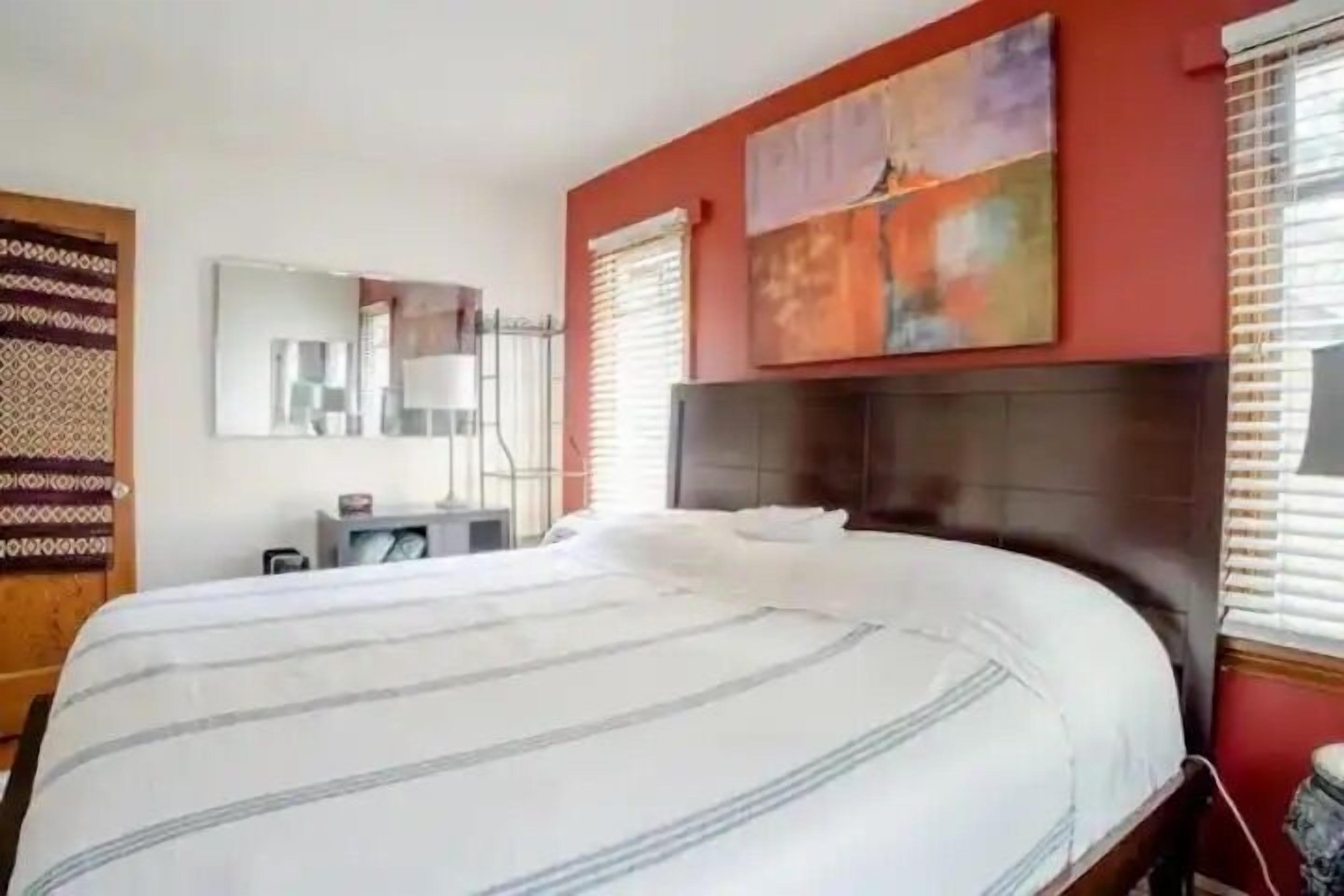 Habitación de hotel con una cama grande, una mesita de noche, un espejo y una ventana con persianas.