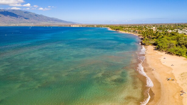 Ein Küstenstrand mit klarem türkisblauem Wasser, einem Sandufer und einer Berg- und Gebäudebäckgrund.