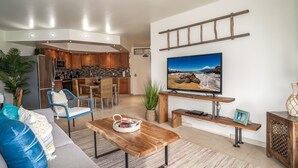 Ein modernes Wohnzimmer mit einer Couch, einem Couchtisch, einem Fernseher und einer Küche im Hintergrund.