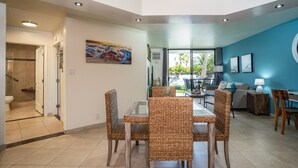 Ein modernes Wohnzimmer mit Essbereich, ausgestattet mit Korbmöbeln, einem Glastisch und Blick ins Freie.