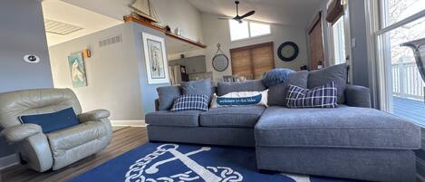 A living room with a sectional sofa, a leather armchair, and a blue rug with an anchor design.