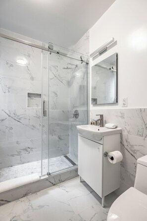 A modern bathroom with a glass-enclosed shower, marble tiles, a white sink, and a toilet.