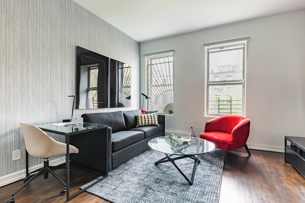 A modern living room with a black sofa, a glass coffee table, a red armchair, and a desk with a chair.