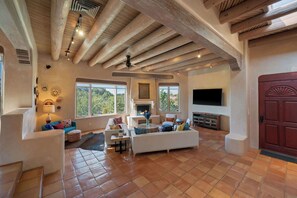 A spacious living room with a fireplace, large windows, and a high ceiling with exposed beams.