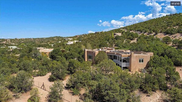 A modern building with a flat roof and multiple windows, surrounded by dense greenery and hills in the background.