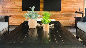 Un coin salon accueillant avec un mur en bois, deux panneaux noirs et une table centrale agrémentée de deux plantes en pot.