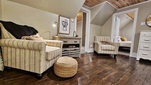 Une chambre à coucher confortable, aménagée en mezzanine, avec un plafond en pente, un fauteuil à rayures, un petit pouf et un lit agrémenté d’un coussin jaune.