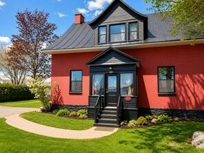 Et rødt murhus med sort hoveddør, en lille veranda og en postkasse.