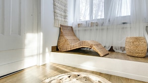 A room with a wooden floor, a woven chair, a woven stool, and a large woven rug.