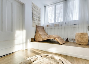 A room with a wooden floor, a woven chair, a woven stool, and a large woven rug. - Maison Jean: at the beach on the St. Lawrence River (batiscan)