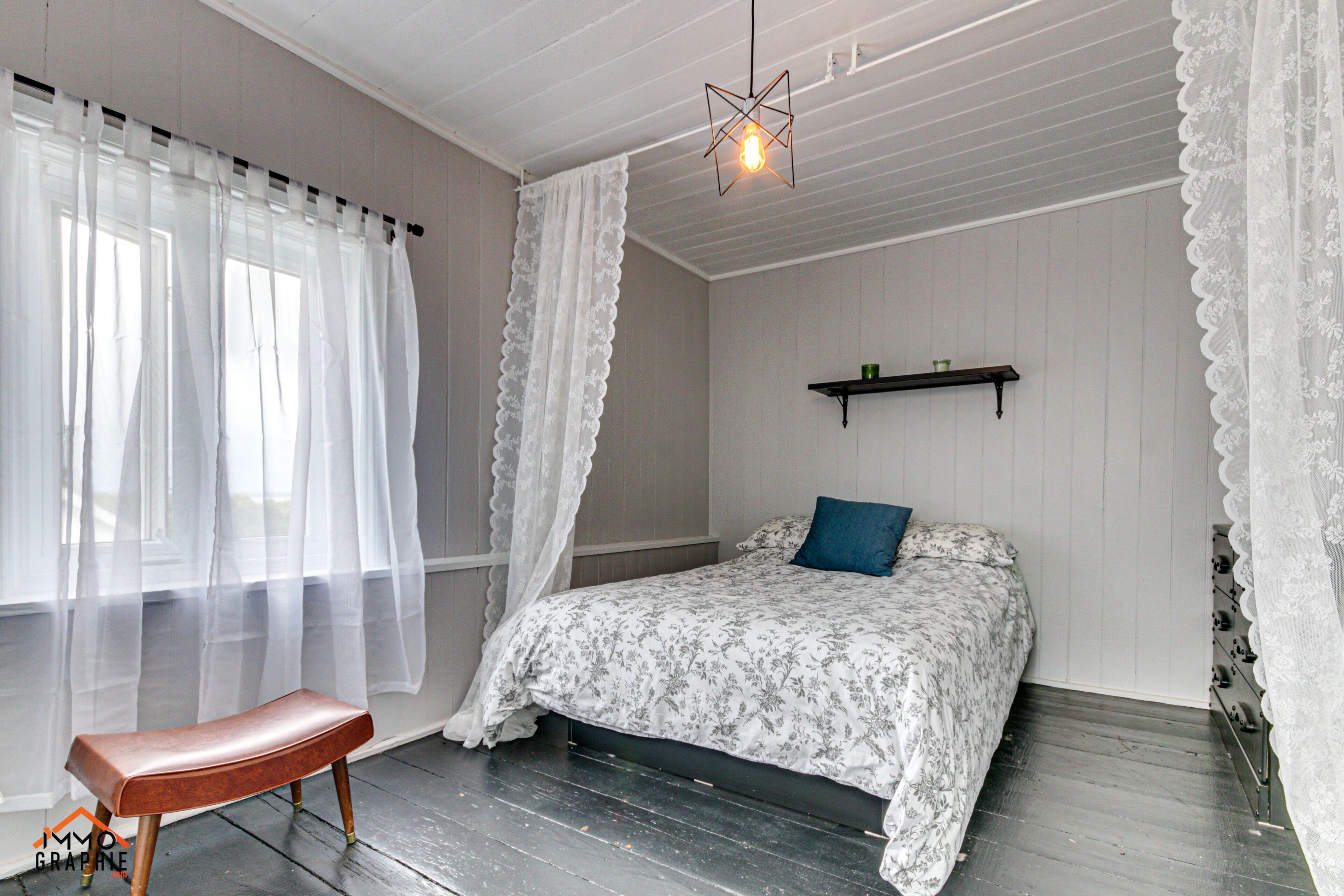 Een slaapkamer met een bed, een bankje, een hanglamp en een plank.