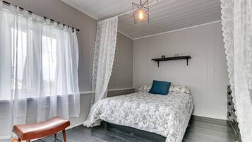 Een slaapkamer met een bed, een bankje, een hanglamp en een plank.