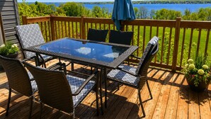 Une terrasse en bois avec une table en verre et des chaises en osier, donnant sur un lac.