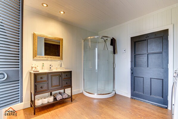 A bathroom with a glass shower enclosure, a vanity with drawers, and a door.