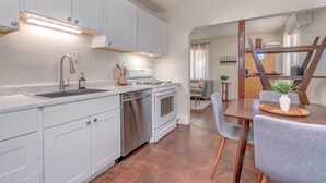A modern kitchen with white cabinets, stainless steel appliances, and a dining area with a wooden table and grey chairs. - ZonaMod MidCentury ⁜King ⁜FirePit ⁜Backyard ⁜Dog Friendly ⁜Near Downtown (Tucson)
