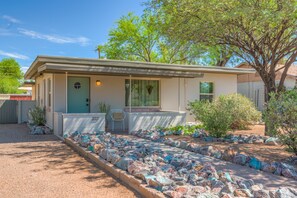 A single-story house with a front porch, a small garden with rocks and plants, and a tree to the right. - ZonaMod MidCentury ⁜King ⁜FirePit ⁜Backyard ⁜Dog Friendly ⁜Near Downtown (Tucson)