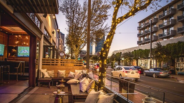 An outdoor seating area with cushioned benches and tables, a wooden fence, and a view of the street with cars and buildings. - ZonaMod MidCentury ⁜King ⁜FirePit ⁜Backyard ⁜Dog Friendly ⁜Near Downtown (Tucson)
