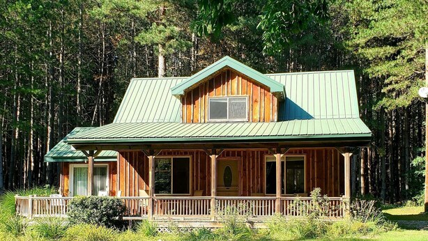 A wooden cabin with a green roof, a porch, and a view of a forest. - The Classic Cottage - Only one mile from the dunes! (Mears)