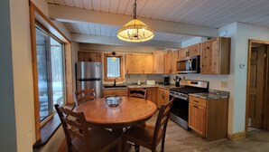 A kitchen with wooden cabinets, a stainless steel refrigerator, a microwave, a stove, and a dining table with chairs. - The Classic Cottage - Only one mile from the dunes! (Mears)