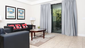A modern living room with a black sofa, two framed artworks, a small table with a plant, and a sliding glass door leading to a balcony. - Premium Villa at Champions Gate (Davenport)