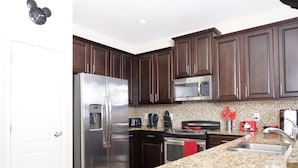 A modern kitchen with dark wooden cabinets, stainless steel appliances, and a granite countertop. - Premium Villa at Champions Gate (Davenport)