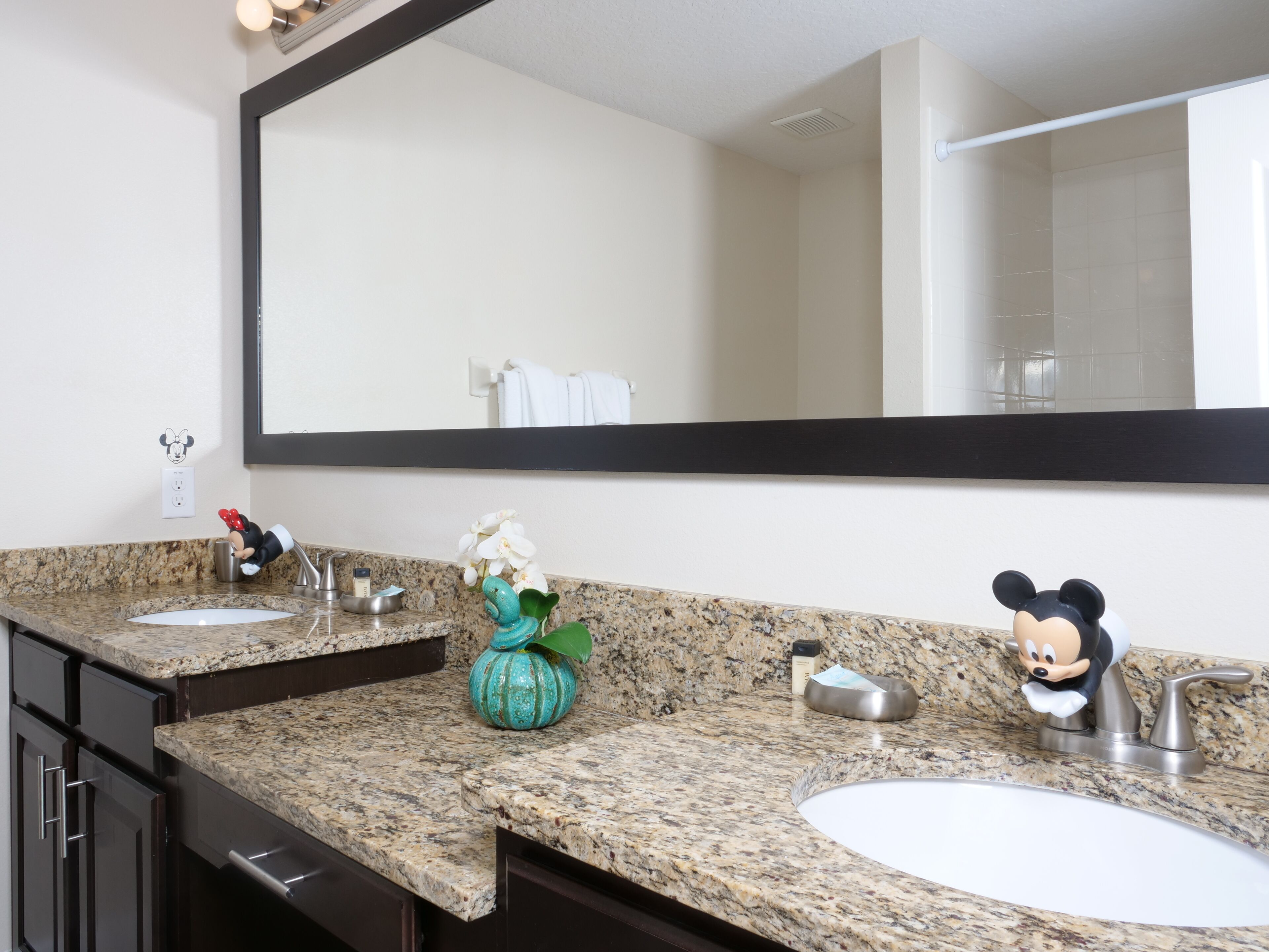 Casa de banho com duas pias, um espelho grande e uma figura do Mickey Mouse no balcão.
