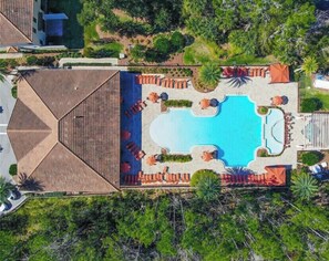 Vista aérea de un complejo turístico con una piscina central, rodeado de zonas de descanso y un edificio grande con un techo distintivo.