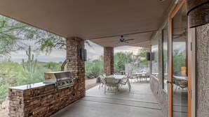 An outdoor patio with a stone barbecue and dining area, surrounded by vegetation and a clear view of the desert landscape. - Golf & Mt VIEWS, Golfers/Hikers Paradise, Comm Htd Salt POOL & Spa, All King Beds (Gold Canyon)