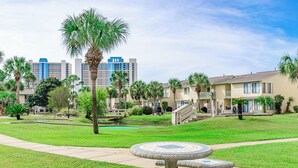 A courtyard with a mosaic fountain, palm trees, and a pool. - Beach Daze Sleeps 6 @ Gulf Highlands Dog Friendly (Panama City Beach)