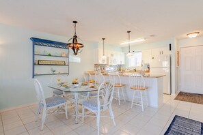 A modern kitchen with white cabinetry, a central island, and a dining area with white chairs and a glass table. - Beach Daze Sleeps 6 @ Gulf Highlands Dog Friendly (Panama City Beach)