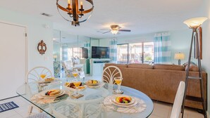 A dining area with a glass table, white chairs, and a brown sofa. - Beach Daze Sleeps 6 @ Gulf Highlands Dog Friendly (Panama City Beach)