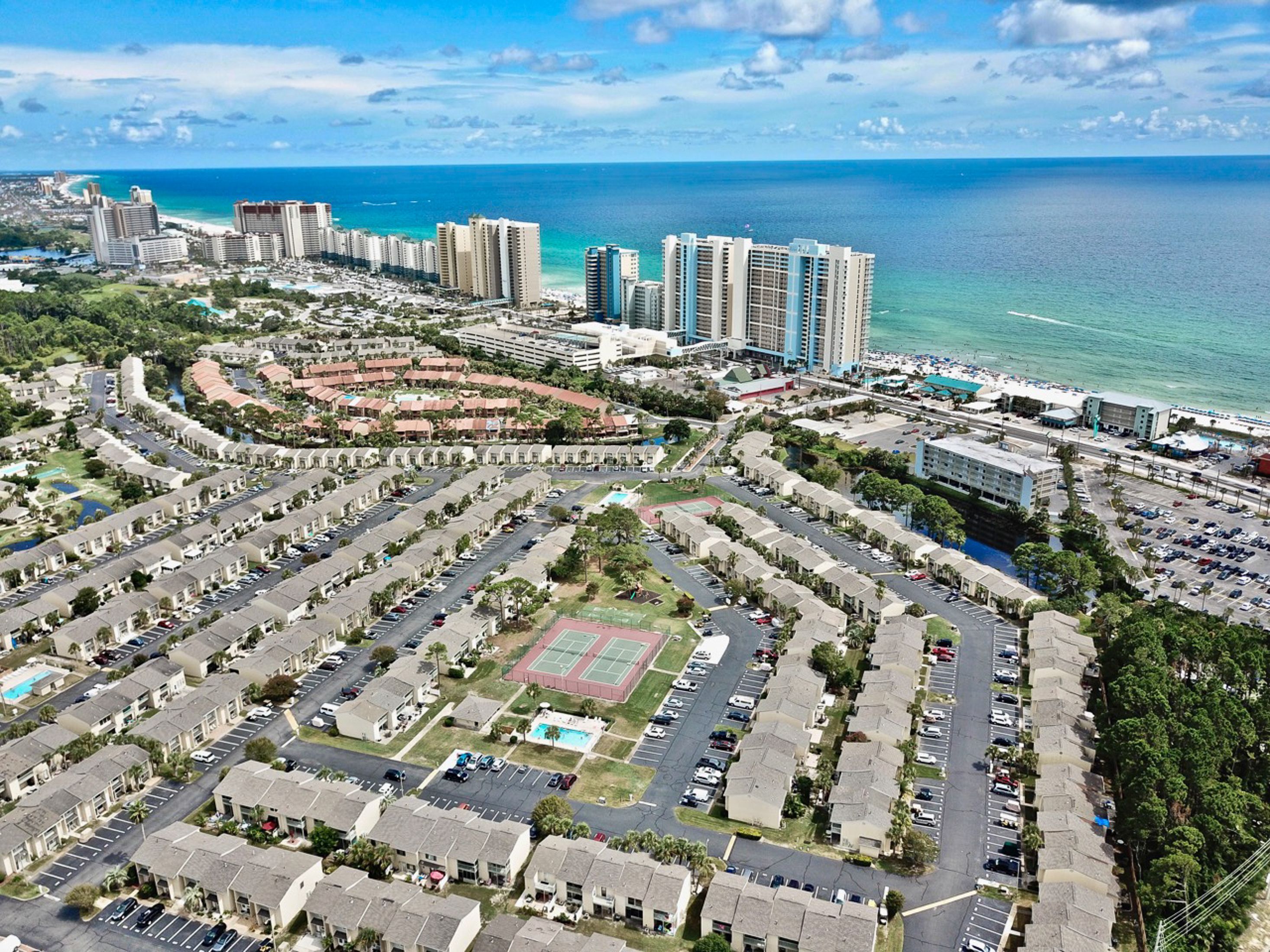 Vista aèria d'una ciutat costanera amb edificis alts, una zona de pàrquing central i un camp esportiu.