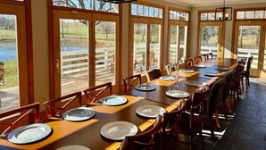 A long dining table set for a meal with chairs, large windows, and a view of a lake.