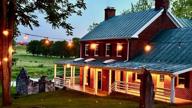A brick building with a metal roof, a covered porch, and string lights.