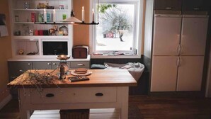 Une cuisine avec une table en bois, des placards blancs, une fenêtre donnant sur un paysage enneigé et un réfrigérateur.