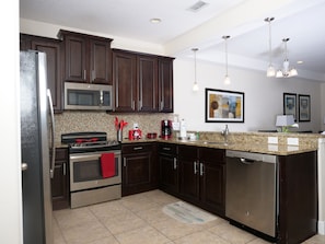 A modern kitchen with dark wood cabinets, stainless steel appliances, a granite countertop, and pendant lighting. - Beautiful Villa in Champions Gate (Davenport)
