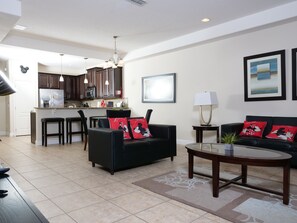 A modern living room with a black sofa, a coffee table, and a kitchen in the background. - Beautiful Villa in Champions Gate (Davenport)
