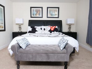 A neatly arranged bedroom with a tufted headboard, a grey upholstered bench, and two framed artworks above the bed. - Beautiful Villa in Champions Gate (Davenport)