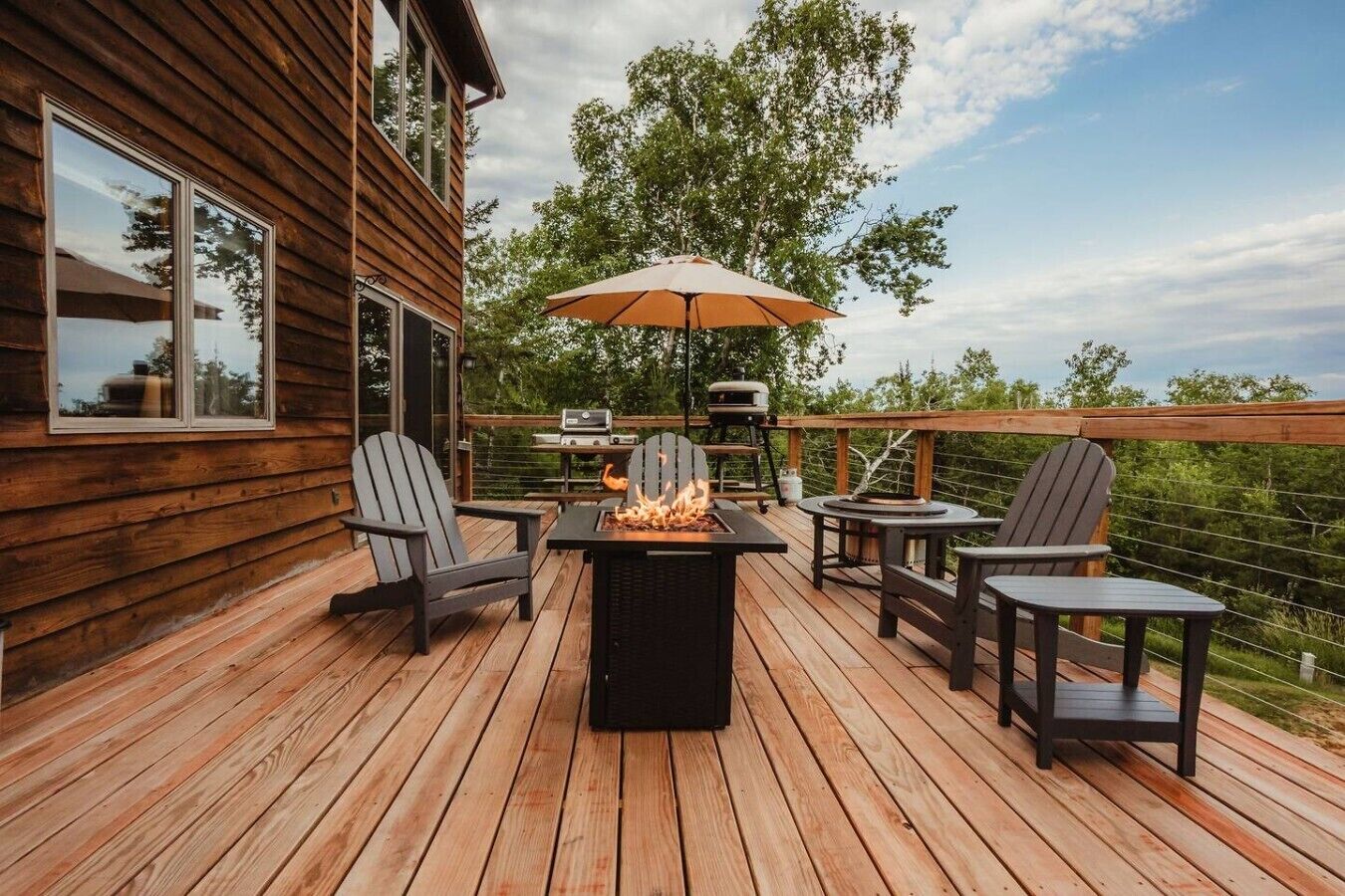 A wooden deck with a fire pit, outdoor furniture, and a grill.