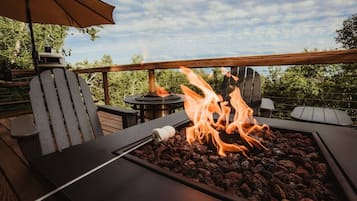 A deck with a fire pit, outdoor seating, and a view of trees.