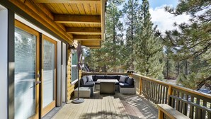 A wooden deck with a built-in seating area, large windows, and a view of trees.