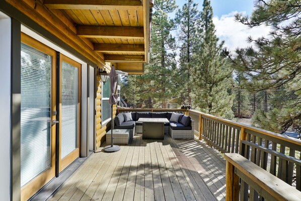 Une terrasse en bois dotée d’un espace salon intégré, de grandes fenêtres et d’une vue sur les arbres.