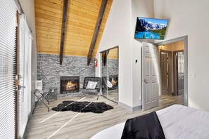 Une chambre moderne avec un mur en pierre, des poutres en bois au plafond, une cheminée, une télévision et un lit.