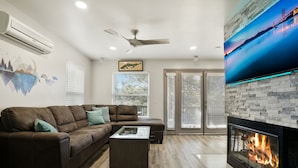 A modern living room with a brown leather sofa, a coffee table, a fireplace, and a large TV mounted on the wall.