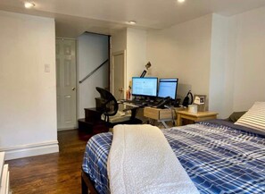 A bedroom with a bed, two monitors on a desk, a chair, and a desk lamp. - Best studio in the heart of West Village! (New York)